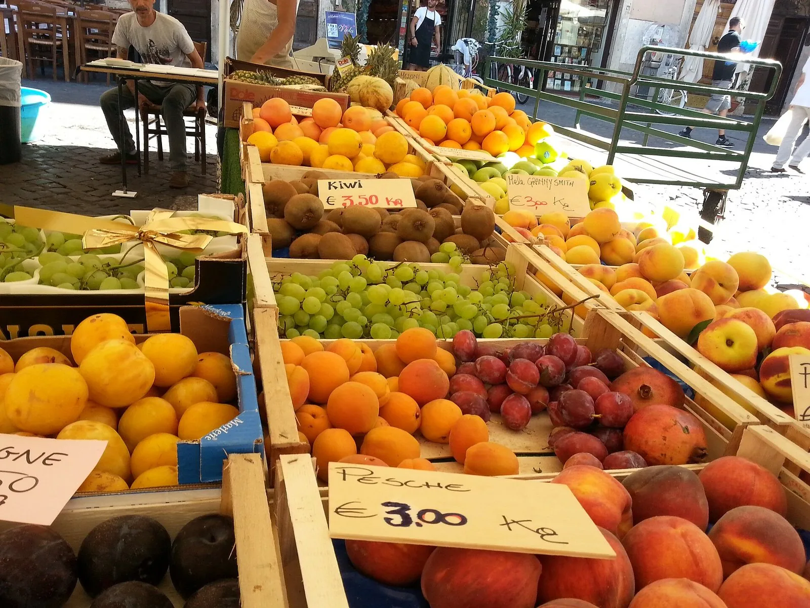 Banchi di frutta e verdura in un mercato di strada a Roma, con cassette di agrumi e pesche