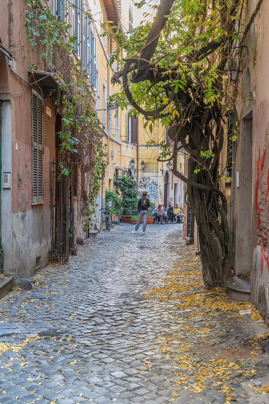 Un vicolo di Roma pavimentato in sampietrini, con le foglie gialle cadute a terra